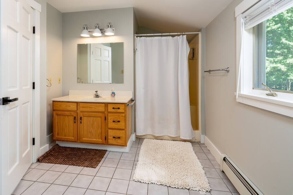 A bathroom with a wooden vanity, a white shower curtain, and a window with a view of trees.
