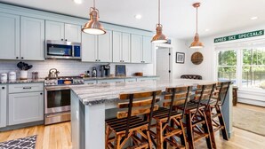 A modern kitchen with light blue cabinets, stainless steel appliances, and a central island with wooden chairs. - Expansive Stowe home, amazing location and hot tub (Stowe)