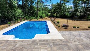 A rectangular swimming pool with a tiled deck, surrounded by a landscaped garden with various plants and trees. - Expansive Stowe home, amazing location and hot tub (Stowe)