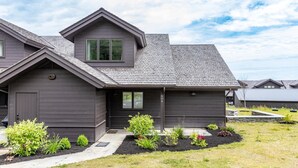 A modern two-story house with a grey exterior, a small front porch, and a well-maintained garden with various plants. - Stunning Trapp Lodge Townhouse, Brand New in Stowe (Stowe)