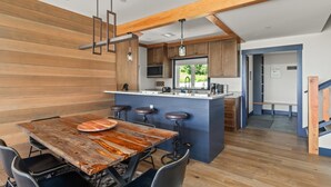 A modern kitchen with wooden cabinetry, a central island with stools, and a view to the outdoors. - Stunning Trapp Lodge Townhouse, Brand New in Stowe (Stowe)