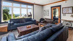A modern living room with a large window, leather sofas, a wooden coffee table, and a bicycle wheel mounted on the wall. - Stunning Trapp Lodge Townhouse, Brand New in Stowe (Stowe)