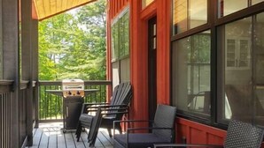 Un portico riparato con pavimento in legno, mobili da esterno neri e un barbecue.