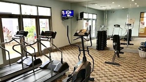 Une salle de sport équipée de tapis de course, de vélos elliptiques et d’un téléviseur fixé au mur.