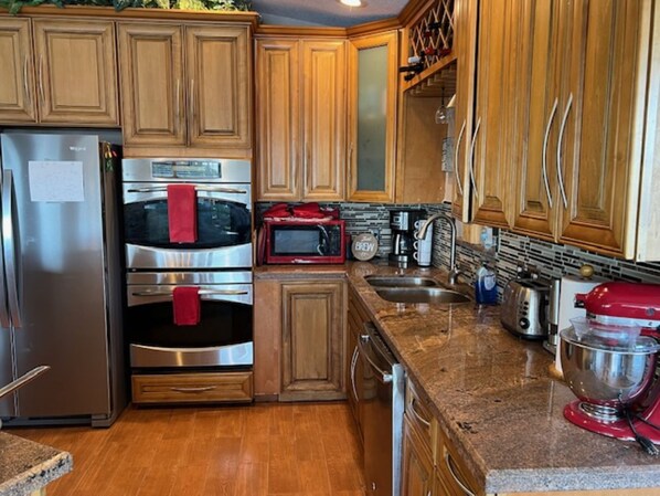Una cocina con gabinetes de madera, electrodomésticos de acero inoxidable, encimera de granito y una batidora de pie roja.