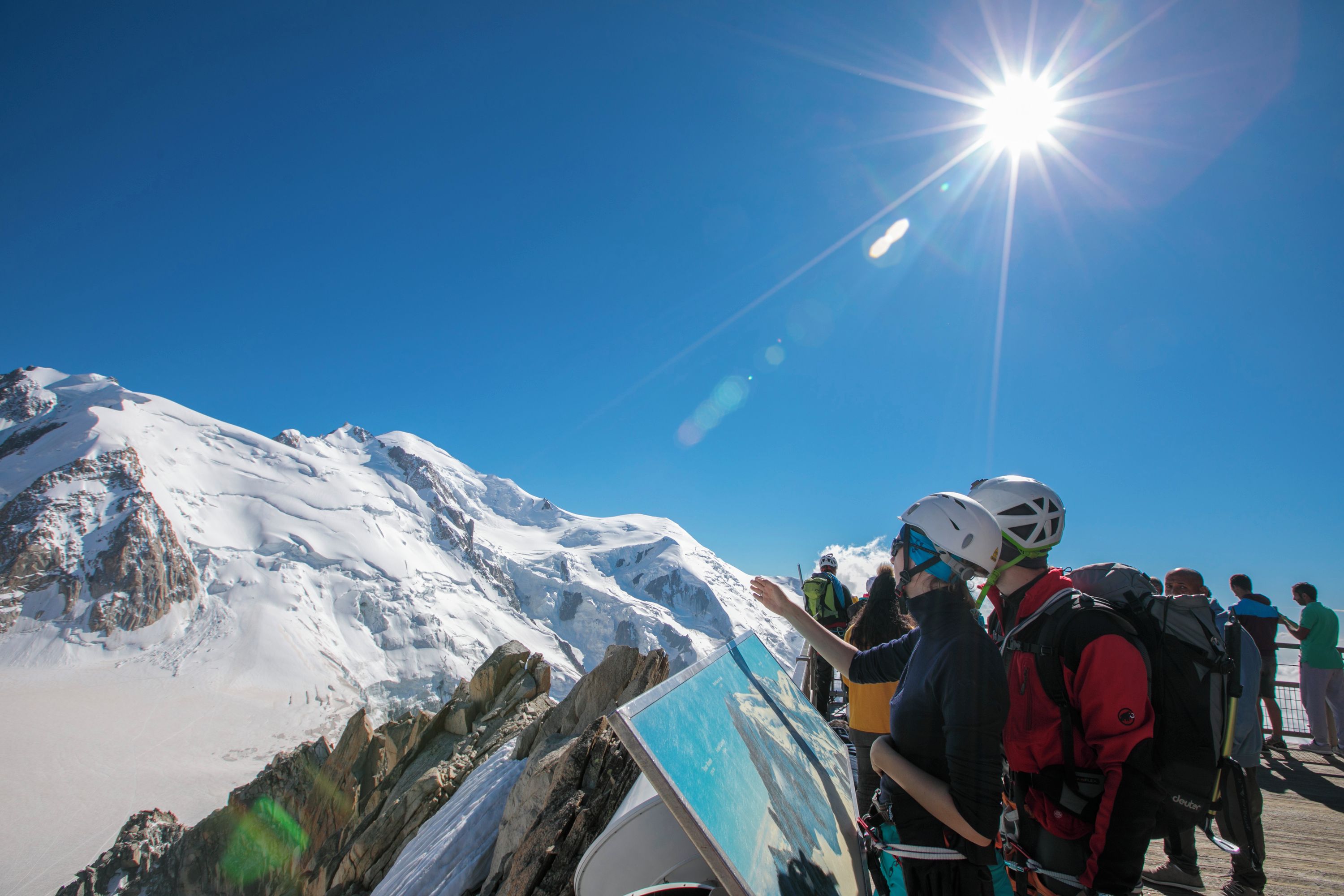 Een groep mensen op een besneeuwde berg met een heldere lucht en fel schijnend zonlicht.