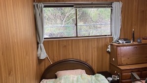 A bedroom with a wooden headboard, a bed with floral bedding, a dresser, and a window with curtains. - Piano Guest House (Sango)