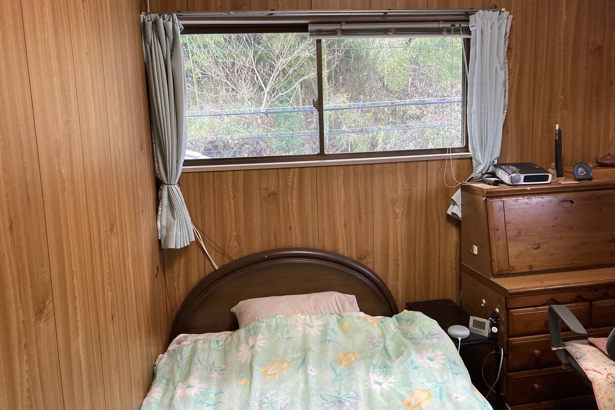 A bedroom with a wooden headboard, a bed with floral bedding, a dresser, and a window with curtains.