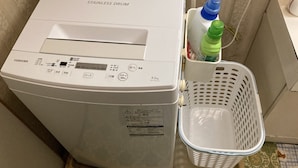 A stainless steel drum washing machine with a control panel, a water bottle, and a laundry basket. - Piano Guest House (Sango)