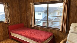 A room with a single bed, wooden walls, a window with curtains, and a chair. - Piano Guest House (Sango)