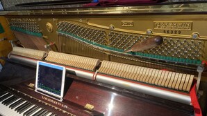 A grand piano with a digital screen displaying a music score. - Piano Guest House (Sango)