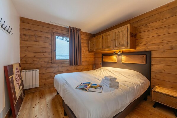 Ein Schlafzimmer mit Holzwänden, einem Bett, einem Fenster, einem Heizkörper und einem Nachttisch.