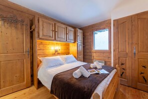 A wooden cabin-style bedroom with a bed, pillows, towels, and a window.
