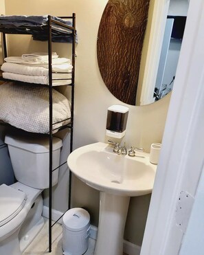 A compact bathroom with a white sink, a toilet, a shelf with folded towels, and a soap dispenser.