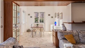 A spacious living area with a patterned sofa, a wooden coffee table, and a dining table with chairs. A large window provides natural light and a view of the outdoors. - Betulla by Interhome (Dervio)