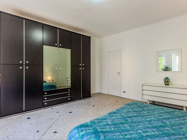 Een slaapkamer met een grote inbouwkast, een bed met een decoratieve spreideken, een nachtkastje met een lamp en een kleine vaas op een dressoir.