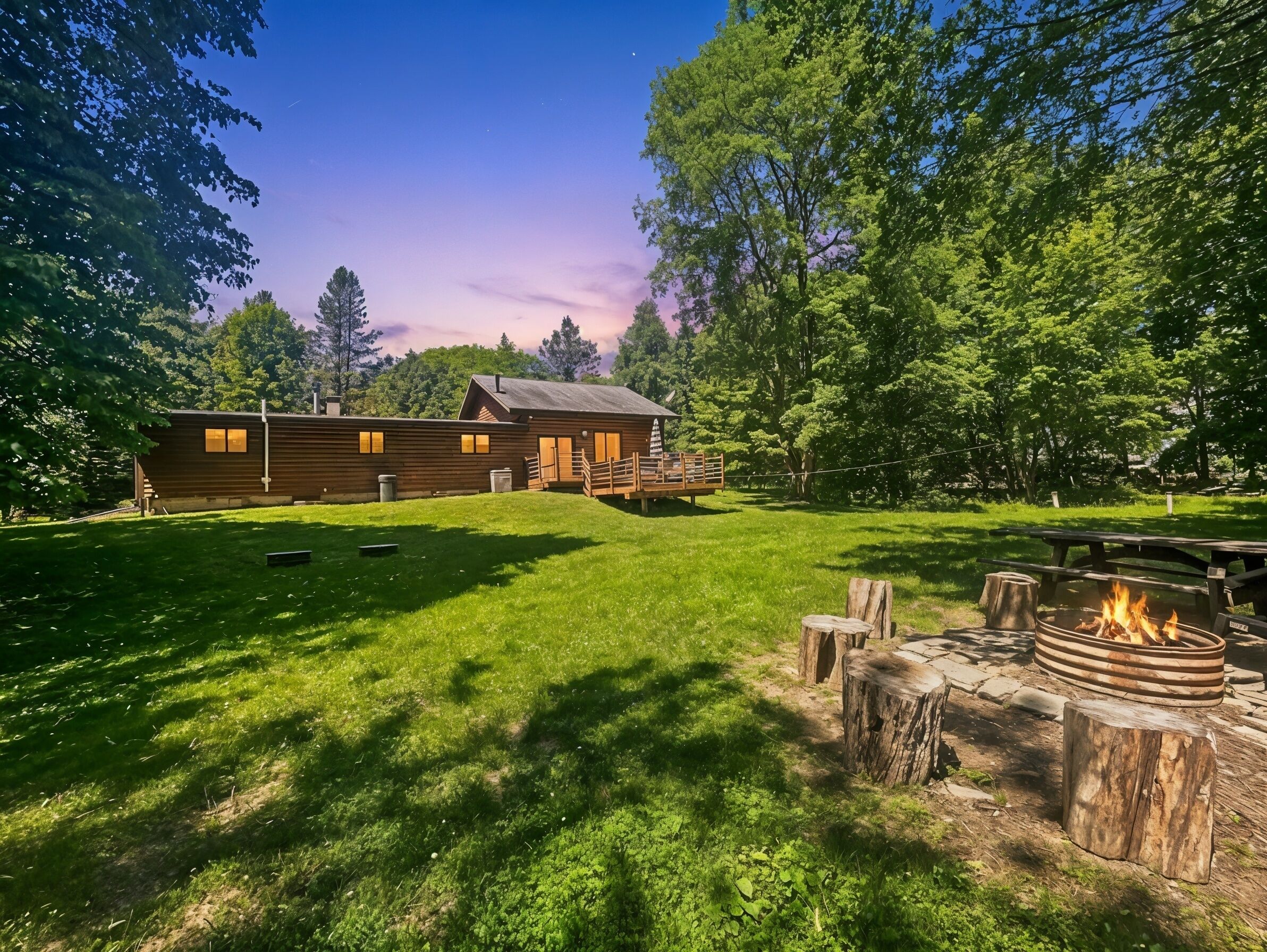 Une cabane en bois dotée d’une terrasse, entourée d’une cour verdoyante et d’arbres.
