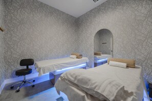 Habitación de hotel con dos camas, una silla, un espejo y un papel tapiz estampado.