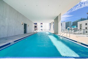 En swimmingpool med kristallklart blått vatten, omgiven av en betongplattform och en vit vägg.
