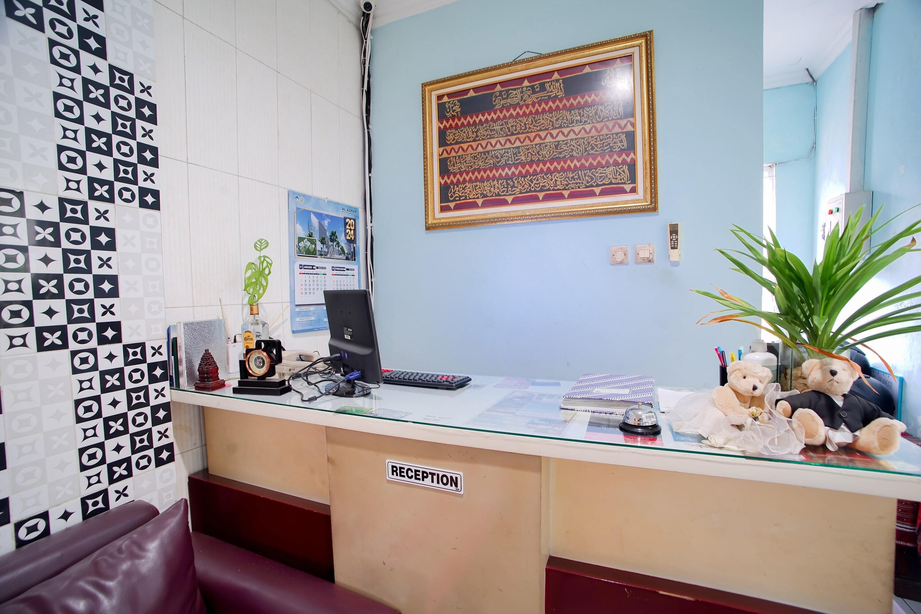 A reception desk with a 'RECEPTION' sign, a computer, a calendar, and decorative items including teddy bears.