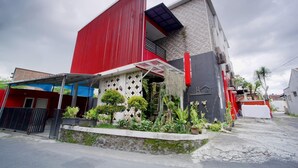 Un bâtiment moderne à la façade rouge, doté d’un balcon et d’un espace jardin agrémenté de diverses plantes.