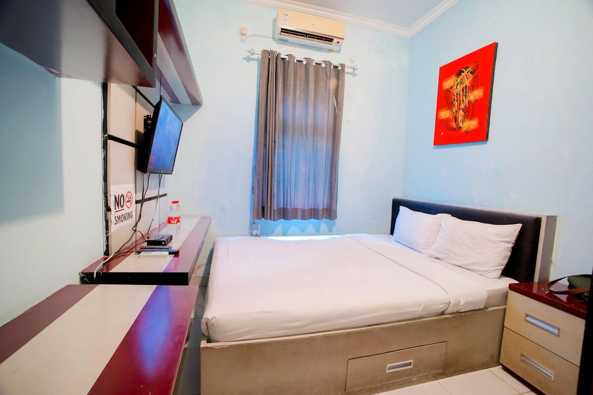 Een hotelkamer met een bed, een bureau met een computer, een televisie en een schilderij aan de muur.