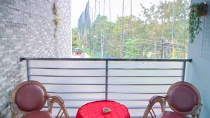 Un balcon avec deux chaises en bois et une petite table recouverte d’une nappe rouge.