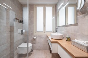 Un baño moderno con cabina de ducha de vidrio, un lavabo blanco y un espejo grande.