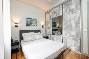 Un dormitorio moderno con una cama grande, una mesita de noche, un espejo e iluminación en la pared.
