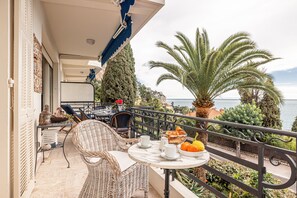 Un balcón con muebles de mimbre, una mesa con tazas y un frutero, y vista al mar.