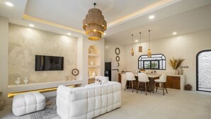 Una sala de estar moderna con un sofá blanco, una zona de comedor con una isla de cocina y un ventanal grande.