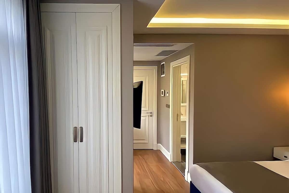Quarto de hotel moderno com piso de madeira, uma cama, um guarda-roupa e um corredor que leva a outro quarto.