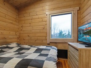 Quarto de cabana de madeira com uma cama, cômoda e janela com vista para uma floresta.