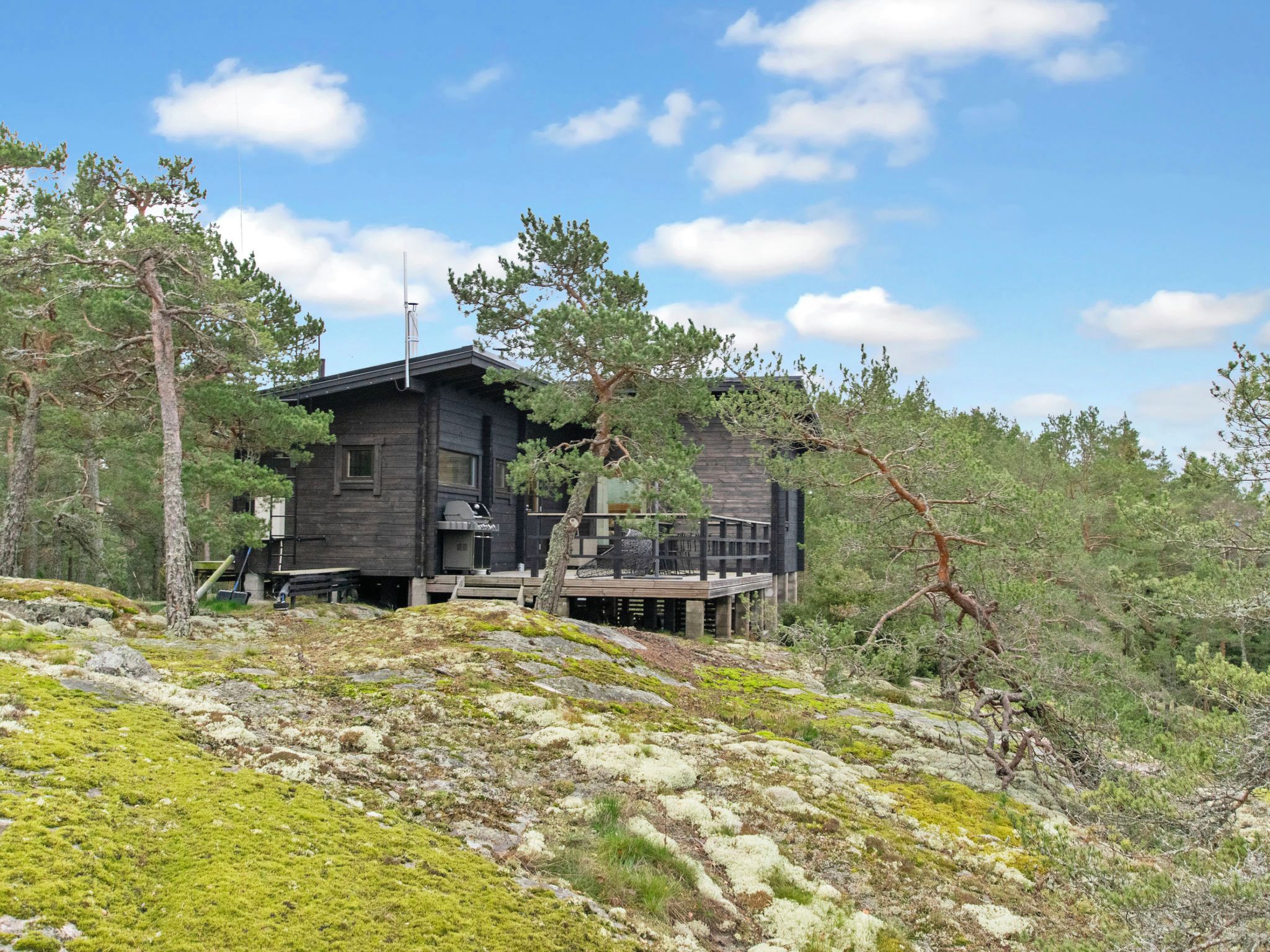 A cabin with a deck, surrounded by trees and a rocky landscape.