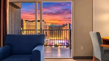A room with a view of a cityscape at sunset, a blue sofa, and a wooden chair.