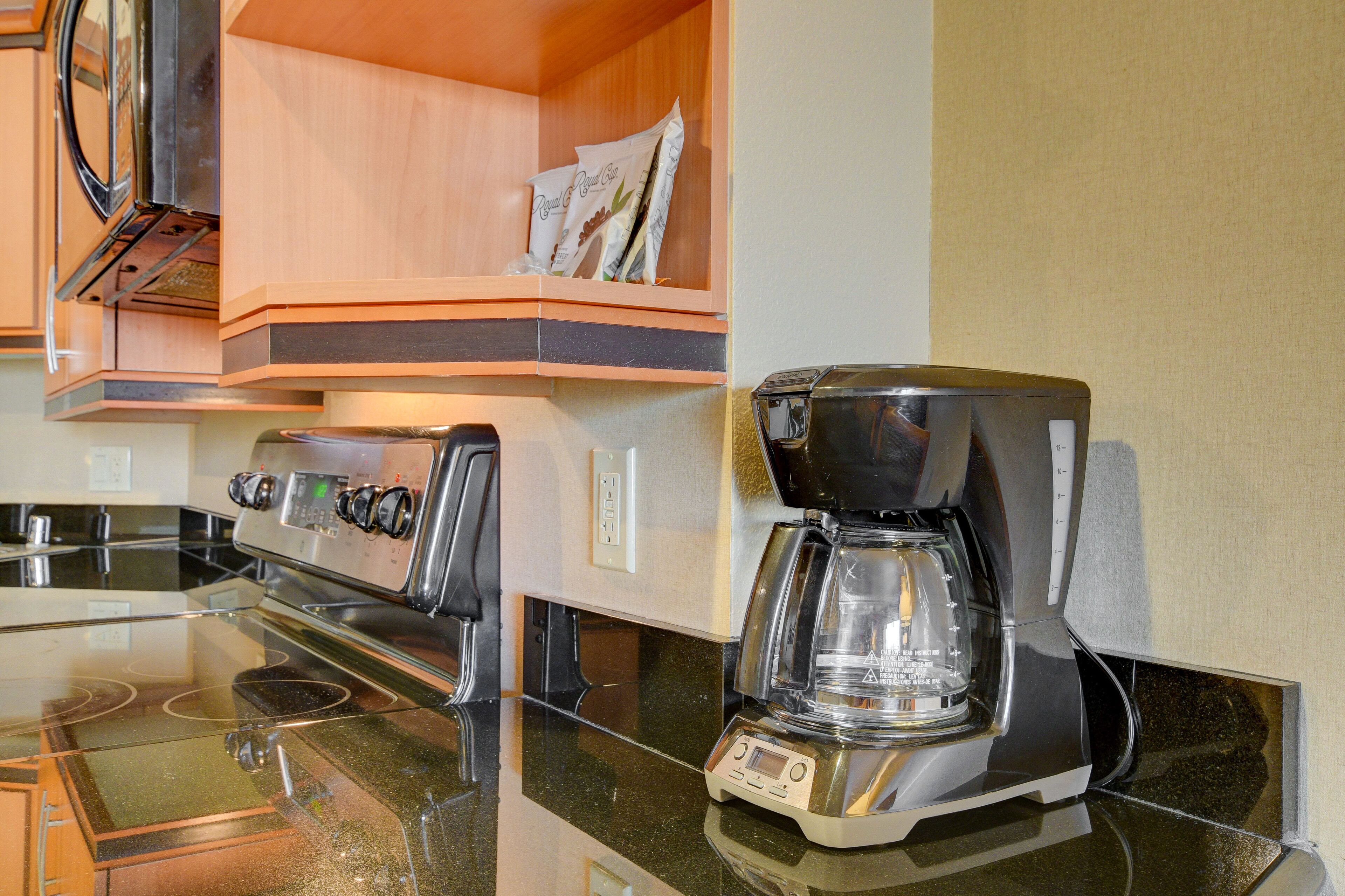 Una cocina con estufa, cafetera y una alacena con alimentos envasados.