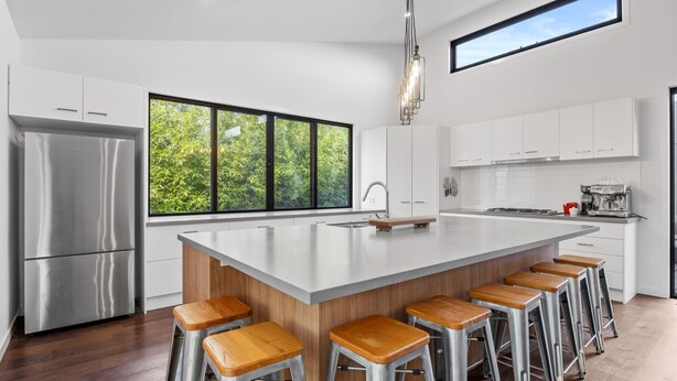 A modern kitchen with a large island, stainless steel appliances, and a view of greenery through the windows. - Sandy Feet Retreat Inverloch (Inverloch)