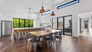 A modern kitchen with a large island, stainless steel appliances, and a view of greenery through the windows. - Sandy Feet Retreat Inverloch (Inverloch)
