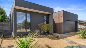 A modern two-story house with large windows, a garage, and a well-maintained garden with gravel and plants. - Sandy Feet Retreat Inverloch (Inverloch)