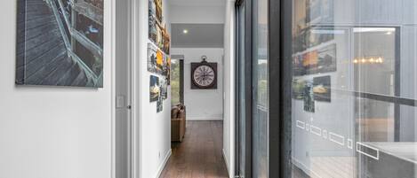 A hallway with a wooden floor, a large clock on the wall, and various framed pictures.