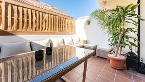 Eine Terrasse mit Glastisch, Korbmöbeln und Topfpflanzen.