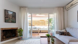 Ein Wohnzimmer mit Kamin, einer Couch, einem Couchtisch und Blick auf einen Balkon mit Holzlattenzaun.