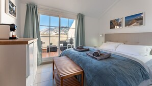Ein Hotelzimmer mit Bett, einer Holzbank, einer Kaffeemaschine und Blick auf Stadt und Berge durch große Fenster.