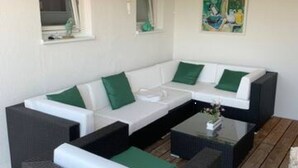 Un espace de détente extérieur moderne, comprenant un canapé d’angle, deux fauteuils, une table basse en verre et une terrasse en bois.