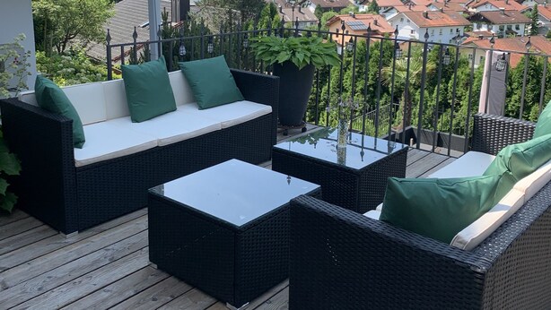 Un balcon agrémenté de meubles en osier, d’une plante en pot et offrant une vue sur la ville et les collines.