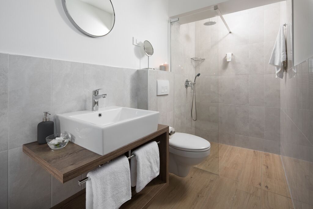 Un bagno moderno con un lavandino bianco grande, uno specchio, un water e una cabina doccia.