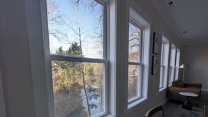 A room with large windows, a sofa, a small table, and a lamp. - Colony Suite - Bridgegate (Marietta)