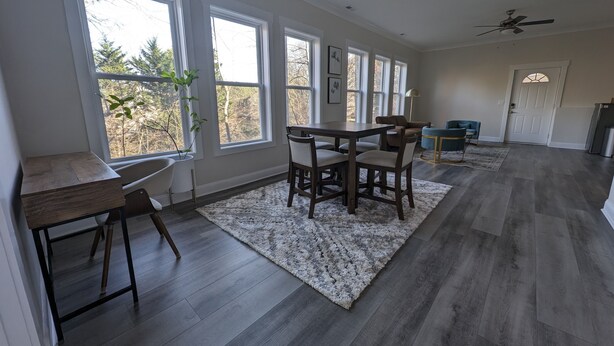 A spacious living room with large windows, a dining area, and a ceiling fan. - Colony Suite - Bridgegate (Marietta)