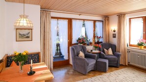 Een gezellige woonkamer met een houten plafond, een tafel met een bloevas, twee fauteuils en uitzicht op een besneeerd landschap door grote ramen.