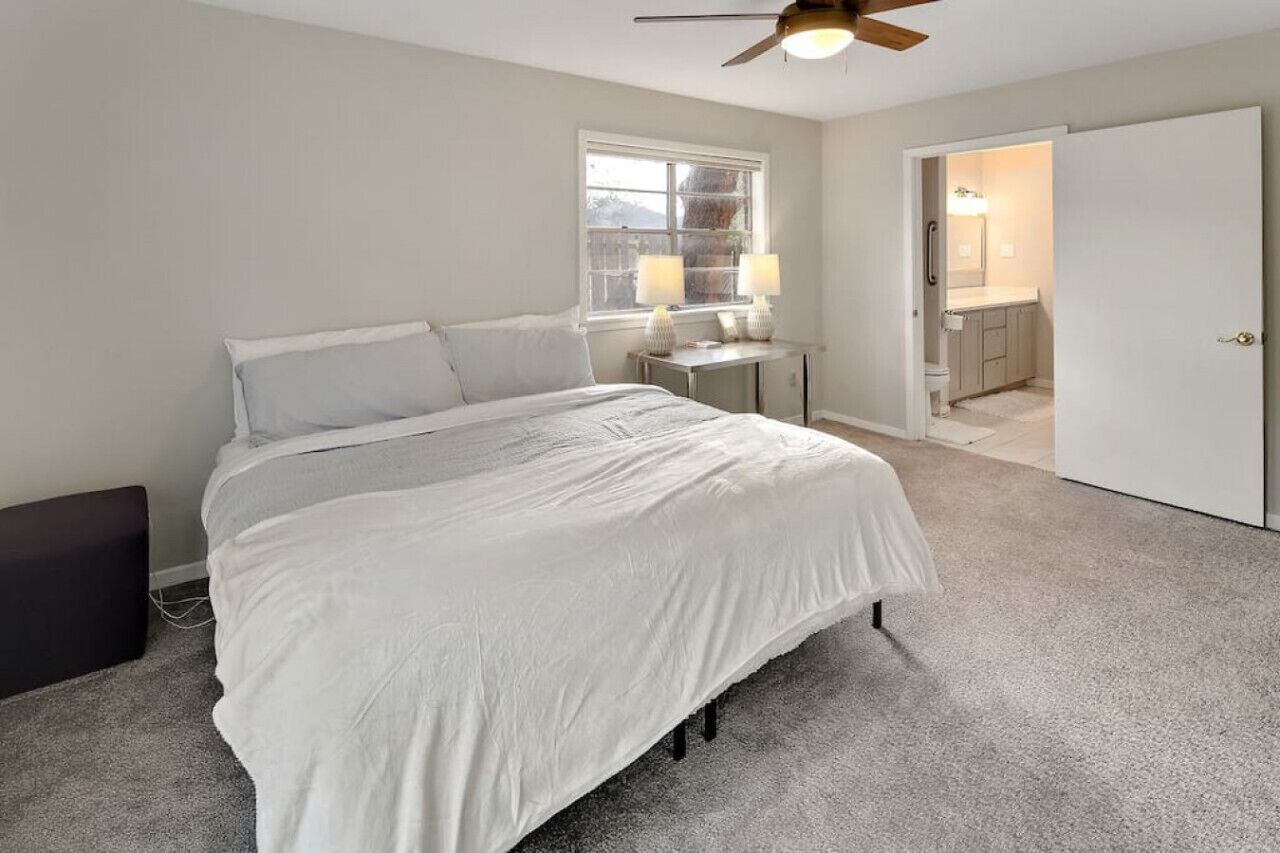 Une chambre à coucher avec un grand lit, une table de chevet, une fenêtre et une porte donnant sur une salle de bain.